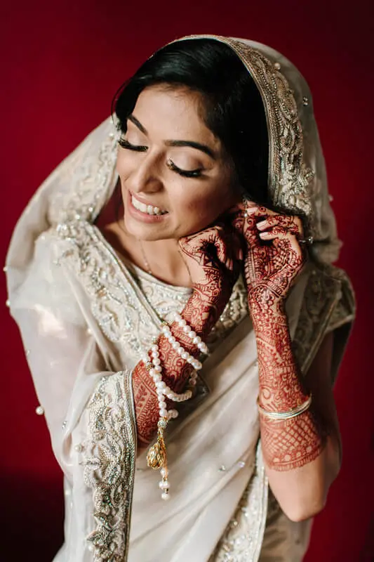 Ivory-clad South Asian bride preparing for wedding ceremony, adjusting earrings in Atlanta