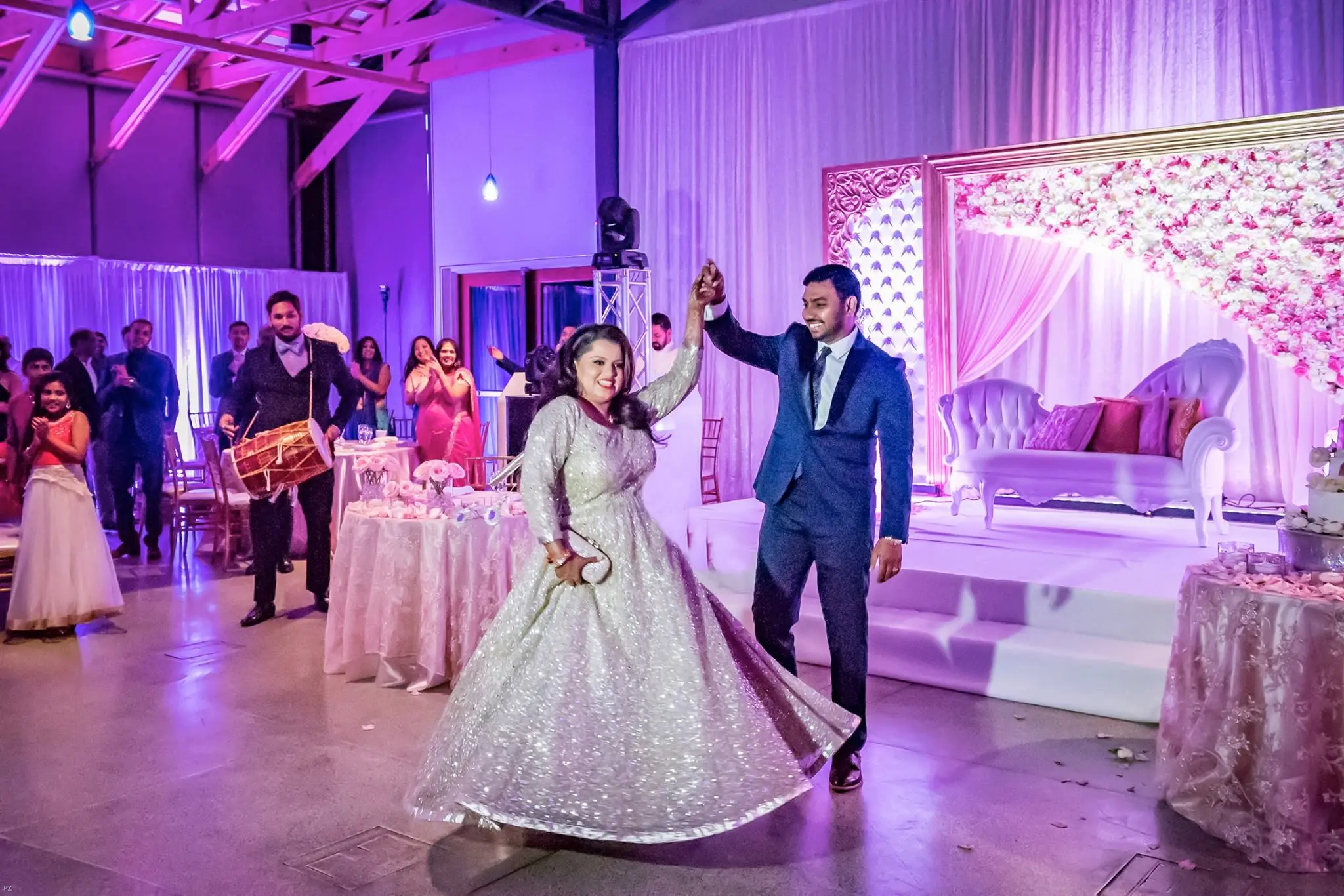 Bride and groom make joyful entrance at South Asian wedding reception in Atlanta under floral décor and pink uplighting