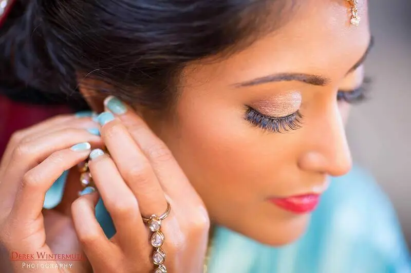 Bride in turquoise outfit preparing for her South Asian wedding in Atlanta, fastening her earring with a reflective expression