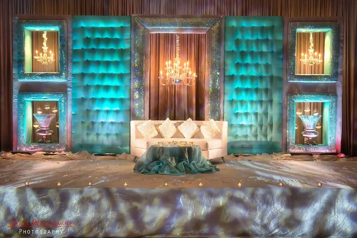 Luxurious fusion wedding stage with teal backdrop, chandeliers, and glittering decor at reception in Georgia